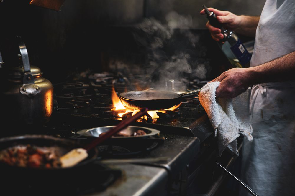 an image from our photoshoot at the restaurant of a chef cooking something on the stove with flames around the pan